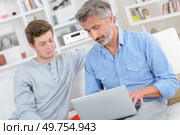 Man using laptop, younger man making facial expression of incomprehension. Стоковое фото, агентство Ingram Publishing / Фотобанк Лори