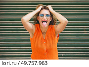Urban portrait of a casual latin cool woman holing her hair and sticking the tongue out smiling. Woman holing her hair and sticking the tongue out smiling. Стоковое фото, агентство Ingram Publishing / Фотобанк Лори