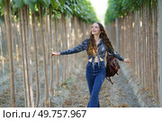 A joyful young woman with long hair strolls through a picturesque grove, savoring natures beauty and fresh air, radiating happiness and freedom, embracing the moment with delight. A Joyful Young Woman Happily Walking Among Tall Trees in Beautiful Nature Surroundings. Стоковое фото, агентство Ingram Publishing / Фотобанк Лори