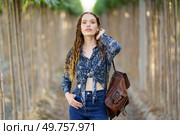 A confident young woman in a stylish denim outfit holds a chic backpack, surrounded by serene nature. Her bright smile and relaxed demeanor reflect a carefree summer lifestyle, embodying adventure. A Confident Young Woman Dressed in Trendy Denim with a Stylish Backpack in a Serene Nature Setting. Стоковое фото, агентство Ingram Publishing / Фотобанк Лори
