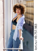 Hot female with brown curly hair in unbuttoned shirt and black bra leaning on railing of balcony looking at camera. Attractive woman with unbuttoned shirt standing on balcony. Стоковое фото, агентство Ingram Publishing / Фотобанк Лори