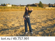 In a sunlit golden field, a young woman beams with joy as she waves cheerfully, dressed in a trendy denim outfit that perfectly embodies a warm and relaxed vibe, radiating happiness and freedom. A Young Woman Dressed in a Stylish Denim Outfit Waves Cheerfully in a Beautiful Golden Field. Стоковое фото, агентство Ingram Publishing / Фотобанк Лори