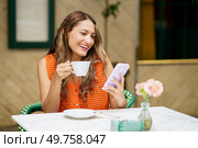 Frontal photo of a happy and relaxed latin woman smiling while using mobile phone in a cafeteria. Latin woman smiling while using mobile phone in a cafeteria. Стоковое фото, агентство Ingram Publishing / Фотобанк Лори