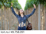 A cheerful and joyful woman stands confidently in a vibrant and lush green aisle, with her arms raised high in pure joy, surrounded by stunning, verdant foliage and towering trees. A Joyful Woman is Deeply Embracing Nature while Surrounded by a Lush Green Aisle of Life and Beauty. Стоковое фото, агентство Ingram Publishing / Фотобанк Лори