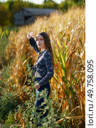 A young woman stands confidently in a vast cornfield, showcasing the latest fall fashion trends against a stunningly beautiful rural backdrop, perfectly blending style with natures charm. A Woman is Posing Beautifully in a Vibrant Cornfield During the Enchanting Golden Hour. Стоковое фото, агентство Ingram Publishing / Фотобанк Лори