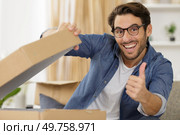 happy man opening parcel box at home showing thumb up. Редакционное фото, агентство Ingram Publishing / Фотобанк Лори