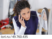young woman on the phone repairing a bicycle wheel. Стоковое фото, агентство Ingram Publishing / Фотобанк Лори