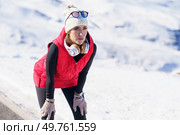 Focused athletic female in warm clothes leaning on knees and breathing after run against snowy mountains in sunlight. Sportive woman resting after jog in winter. Стоковое фото, агентство Ingram Publishing / Фотобанк Лори