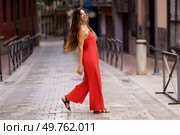 A stylish and confident woman dressed in a vibrant red dress gracefully strolls through a picturesque urban alleyway, showcasing not only her fashion sense but also her undeniable elegance and charm. A Fashionable Woman Dressed in a Stunning Red Dress is Walking Through a Lively Urban Alley. Стоковое фото, агентство Ingram Publishing / Фотобанк Лори