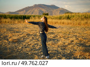 A carefree individual stands in the middle of a vast, open field, arms fully outstretched wide, delighting in the beauty and overwhelming tranquility of nature beneath a stunning mountain backdrop. Free Spirit in Nature Fully Embracing the Beauty of the Open Air and Its Wonders. Стоковое фото, агентство Ingram Publishing / Фотобанк Лори