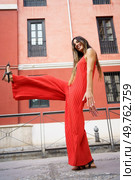 A confident woman in a striking red jumpsuit stands elegantly against a vibrant urban backdrop, showcasing her modern style and charm, capturing the attention of everyone around her. A Stylish Woman in a Vibrant Red Jumpsuit Posing Outdoors While Showcasing Her Beauty and Confidence. Стоковое фото, агентство Ingram Publishing / Фотобанк Лори