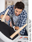 man using sealant gun to repair broken chair. Стоковое фото, агентство Ingram Publishing / Фотобанк Лори