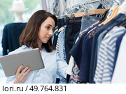 shop keeper holding tablet and looking through rail of clothes. Стоковое фото, агентство Ingram Publishing / Фотобанк Лори