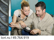 mechanics inflating tire and checking air pressure with gauge. Стоковое фото, агентство Ingram Publishing / Фотобанк Лори