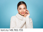 Portrait of young happy beautiful woman smiling and looking away, isolated on blue background in a warm white sweater. Concept of winter promo sale. Стоковое фото, агентство Ingram Publishing / Фотобанк Лори