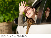 A young woman with a bright smile joyfully waves from a car window, surrounded by lush greenery, capturing the essence of happiness and adventure in her expression during her journey. A Joyful Girl Cheerfully Waving from the Open Window of a Car Surrounded by Beautiful Nature. Стоковое фото, агентство Ingram Publishing / Фотобанк Лори