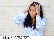 A young woman is clearly showing signs of stress and anxiety, as she holds her head in her hands while leaning against a textured wall, revealing her emotional state and internal struggle. A Stressed Young Woman is Holding Her Head in Discomfort Against a Wall, Struggling With Tension. Стоковое фото, агентство Ingram Publishing / Фотобанк Лори