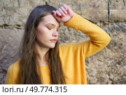 A young woman with flowing, beautiful hair, clad in a bright, vibrant yellow sweater, stands gracefully against an aged stone wall, evoking a sense of introspection, tranquility, and calmness. A contemplative young woman wearing a bright yellow sweater stands gracefully against a stone wall. Стоковое фото, агентство Ingram Publishing / Фотобанк Лори