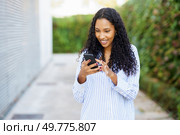 A cheerful young woman with curly hair is intently focused on her smartphone while surrounded by stunning green scenery, which adds to her joy and enhances her carefree spirit and lively demeanor. A young woman happily engaged with her smartphone while enjoying an outdoor setting nearby. Стоковое фото, агентство Ingram Publishing / Фотобанк Лори