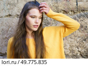 A serene young woman with flowing long hair, wearing a bright and cheerful yellow sweater, poses thoughtfully against a beautifully textured stone wall, exuding a sense of calm and elegance. A contemplative woman dressed in a bright yellow sweater poses against a textured stone wall. Стоковое фото, агентство Ingram Publishing / Фотобанк Лори
