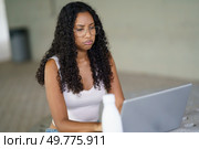 In a contemporary workspace designed for creativity and collaboration, a young woman with curly hair and stylish glasses is focused on her sleek laptop, embodying modern productivity and inspiration. A Focused Woman is Intently Engaged in Productive Work on Her Laptop in a Modern Office Environment. Стоковое фото, агентство Ingram Publishing / Фотобанк Лори