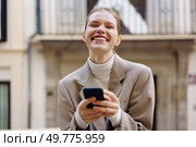 A joyful woman smiles brightly while checking her smartphone in an urban outdoor setting, radiating pure happiness and confidence, making the moment one of connection and delight in life. A Cheerful Woman Happily Using Her Smartphone While Enjoying the Outdoors in the City. Стоковое фото, агентство Ingram Publishing / Фотобанк Лори