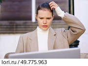 A young, ambitious businesswoman sits in her office, perplexed and contemplative in front of her laptop, deeply focused on solving a challenging technical issue causing her frustration. A Pensive Businesswoman is Struggling with Various Laptop Problems and Technical Issues. Стоковое фото, агентство Ingram Publishing / Фотобанк Лори