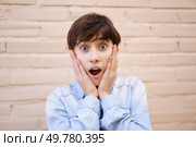 A young girl wears a surprised expression on her face with her hands on her cheeks, expressing a mix of shock and joy as she stands in front of a neutral background that allows her emotions to shine. A Surprised Young Girl Expressing Her Excitement with Genuine Emotion and Enthusiasm. Стоковое фото, агентство Ingram Publishing / Фотобанк Лори