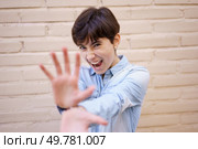A very playful and spirited young woman with short hair poses joyfully and energetically in front of a light brick wall, playfully reaching out her hands while wearing a bright smile on her face. A Joyful and Cheerful Young Woman Playfully Posing Against a Colorful Brick Wall. Стоковое фото, агентство Ingram Publishing / Фотобанк Лори
