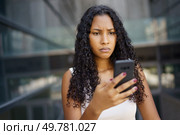 A young woman with curly hair looks worried while checking her smartphone in a busy urban setting, showcasing how modern technology affects our emotions and social interactions daily. A Concerned Woman is Interacting Thoughtfully with Her Smartphone in an Urban Setting. Стоковое фото, агентство Ingram Publishing / Фотобанк Лори