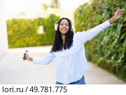 A cheerful young woman dances joyfully outdoors in a stunning vibrant green setting, donning stylish headphones while immersing herself in the rhythm of her favorite music and feeling free. A Joyful Young Woman Happily Enjoying Her Music Outdoors While Wearing Headphones. Стоковое фото, агентство Ingram Publishing / Фотобанк Лори