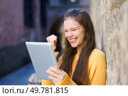 A young woman who is wearing a bright yellow sweater radiates joy as she smiles and celebrates, actively using a tablet, all set against a charming and historic backdrop that adds character. Joyful Young Woman Celebrating on a Tablet in a Beautiful Historic Urban Setting Today. Стоковое фото, агентство Ingram Publishing / Фотобанк Лори