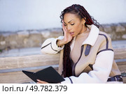A fashionable woman with beautifully braided hair is engrossed in reading an eBook outdoors, displaying a remarkable level of concentration and tranquility in her serene and peaceful environment. A woman reads an electronic tablet comfortably outdoors, enjoying the gentle breeze. Стоковое фото, агентство Ingram Publishing / Фотобанк Лори