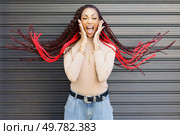 A vibrant woman joyfully poses with her striking red braided hair. She exudes happiness and energy while standing against a lively modern backdrop, embodying a spirited and cheerful essence. An Excited Woman with Striking Red Braids Expressing Pure Joy Against a Stylish Background. Стоковое фото, агентство Ingram Publishing / Фотобанк Лори