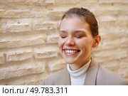 A joyful woman, her eyes gently closed and a bright, radiant smile on her face, poses gracefully against a textured wall, emanating warmth and an uplifting sense of positivity that inspires happiness. A Woman Smiling Joyfully Against a Textured Wall, Radiating Warmth and Happiness. Стоковое фото, агентство Ingram Publishing / Фотобанк Лори