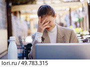 A visibly frustrated young woman finds herself sitting outside, grappling with her laptop and the numerous difficulties that accompany effective remote work in challenging outdoor environments. A frustrated professional is trying to work on a laptop outside, facing many distractions. Стоковое фото, агентство Ingram Publishing / Фотобанк Лори