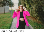 A joyful young woman enjoys her favorite music on a walk outdoors, wearing a vibrant pink blazer and stylish headphones, embodying modern youth and urban fashion in a lively atmosphere. A Happy Young Woman Enjoys Walking Outdoors While Wearing a Bright Pink Blazer and Headphones. Стоковое фото, агентство Ingram Publishing / Фотобанк Лори
