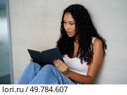 A young woman sits comfortably, fully engaged in her ebook, embodying the ideal themes of leisurely activities, the modern art of reading, and the role of technology in todays lifestyle. A young woman reads an engaging ebook in a cozy space, enjoying her leisure time. Стоковое фото, агентство Ingram Publishing / Фотобанк Лори
