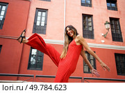 A joyful woman confidently poses in a strikingly vibrant red jumpsuit against a stunning urban backdrop, showcasing not only her fashion sense but also her undeniable confidence and grace. Experience the Joyful Fashion in an Urban Setting featuring Vibrant Red Jumpsuit Photography. Стоковое фото, агентство Ingram Publishing / Фотобанк Лори
