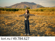A joyful young woman stands with her arms outstretched wide in a serene and beautiful landscape, fully embracing the warmth of the sunlight, surrounded by stunning mountains in the background. A Joyful Woman Embracing Nature Beautifully Set Against a Stunning Mountain Backdrop. Стоковое фото, агентство Ingram Publishing / Фотобанк Лори