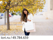 In a charming autumn scene filled with colorful yellow leaves, a cheerful young woman beams with joy as she carries a couple of stylish shopping bags, radiating happiness and positivity. A Young Woman is Happily Enjoying a Delightful Shopping Day in the Beautiful Autumn. Стоковое фото, агентство Ingram Publishing / Фотобанк Лори