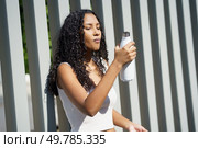 A young woman with curly hair joyfully sips from her stylish, modern water bottle, standing against a vibrant and colorful backdrop, embodying a relaxed lifestyle centered on health and joy. A Young Woman Happily Enjoying Refreshing Hydration While Being Outdoors in Nature. Стоковое фото, агентство Ingram Publishing / Фотобанк Лори