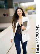 A confident, professional woman strides through an urban setting, carrying a clipboard that showcases her business skills and stylish flair, exuding poise and determination amidst the bustling city. A Confident Business Professional Who is Dressed in a Stylish and Fashionable Outfit. Стоковое фото, агентство Ingram Publishing / Фотобанк Лори