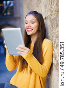 A cheerful young woman wearing a vibrant yellow sweater is happily engaged with her tablet in a picturesque urban setting, savoring a delightful moment of connection, joy, and happiness in her life. A Joyful Young Woman is Engaged with Her Tablet While in a Bustling Urban Setting. Стоковое фото, агентство Ingram Publishing / Фотобанк Лори