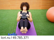 A dedicated woman is currently engaging in a strenuous core workout on her yoga mat, skillfully using a weight plate to add extra resistance and enhance her focus during the exercise routine. A fitness enthusiast is doing a core workout with a weight plate for added resistance. Стоковое фото, агентство Ingram Publishing / Фотобанк Лори