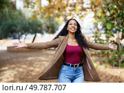In a sunlit park with lush grass and colorful flowers, a joyful woman with curly hair spreads her arms wide, celebrating the beauty of nature and embracing the moment with freedom. A Joyful Woman Embracing Nature in a Beautiful Park Setting Among the First Signs of Autumn. Стоковое фото, агентство Ingram Publishing / Фотобанк Лори