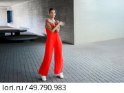 A confident woman poses in a vibrant red jumpsuit that reflects her unique style, against a stunning architectural background, showcasing a blend of modern fashion and timeless elegance. A Stylish Woman in a Red Jumpsuit Posing Confidently Outdoors with an Air of Elegance. Стоковое фото, агентство Ingram Publishing / Фотобанк Лори