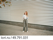 A trendy, fashionable young woman with vibrant red hair stands confidently against a contemporary urban backdrop, showcasing her distinctive and unique fashion sense with great style and flair. A stylish young woman confidently poses against a backdrop of modern architecture. Стоковое фото, агентство Ingram Publishing / Фотобанк Лори