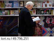 Пожилой мужчина знакомится с содержанием книги на книжной ярмарке в Москве (2022 год). Редакционное фото, фотограф Дмитрий Киселёв / Фотобанк Лори
