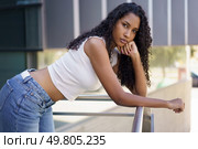 A fashionable young woman with beautiful, curly hair strikes a confident pose against a sleek, modern backdrop. Her casual yet stylish outfit perfectly highlights her chic and trendy sense of fashion. A Stylish Young Woman is Posing Outdoors with her Curly Hair in the Bright Sunlight. Стоковое фото, агентство Ingram Publishing / Фотобанк Лори